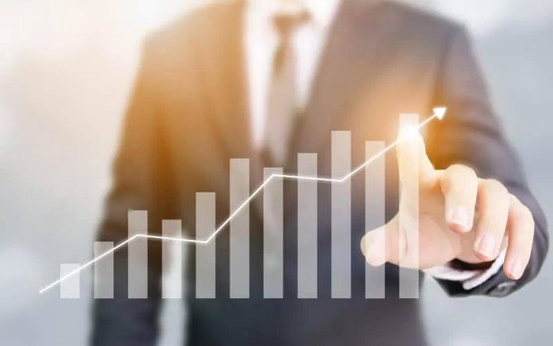A person in a suit points at a virtual graph with rising bar and line charts, illustrating business growth or financial success driven by effective Revenue Cycle Management.