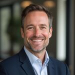 A man in a suit smiles at the camera, standing indoors with a blurred office background—perfect for a professional landing page focused on Medical Record Review services.